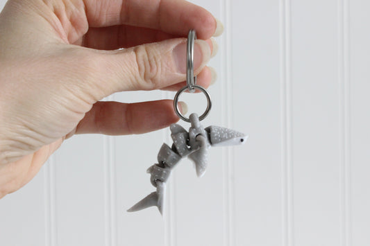 Hand holding the 3D-printed blue-gray whale shark with white spots keychain to show its size, colors, and silver swivel clip.