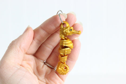 Hand holding the 3D-printed seahorse keychain to show its size, colors, and silver swivel clip.