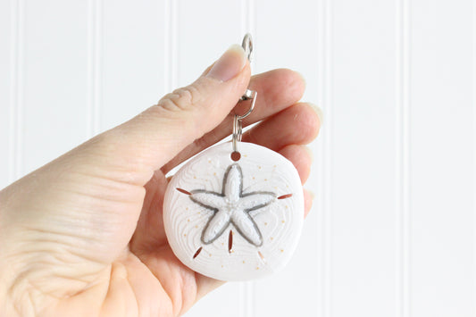 Hand holding the 3D-printed sand dollar keychain to show its size, colors, and silver swivel clip.