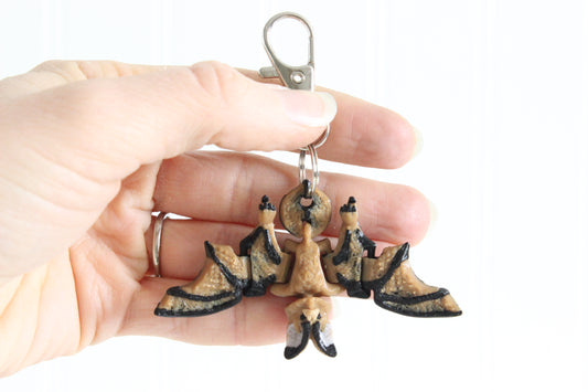 Hand holding a 3D-printed bat keychain to show its size and wing shape.