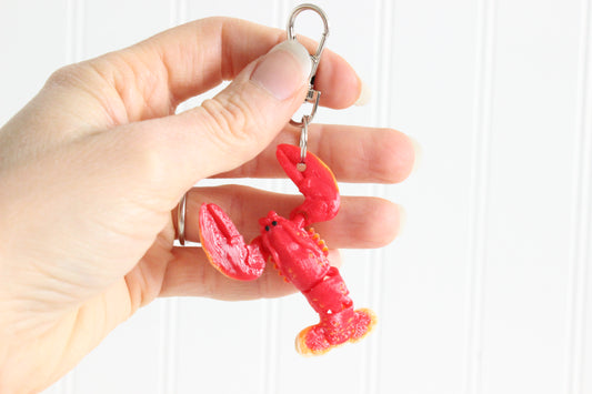 Hand holding the 3D-printed red lobster keychain to show its size, colors, and silver swivel clip.