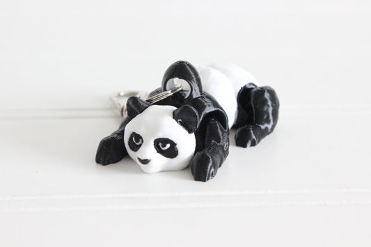 Hand holding the 3D-printed black-and-white panda bear keychain to show its size, colors, and silver swivel clip.