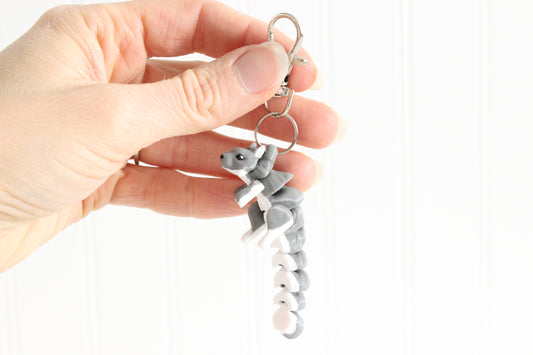 Hand holding the 3D-printed gray squirrel keychain to show its size, colors, and silver swivel clip.
