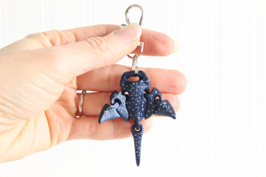 Hand holding the 3D-printed spotted eagle ray with white spots keychain to show its size, colors, and silver swivel clip.