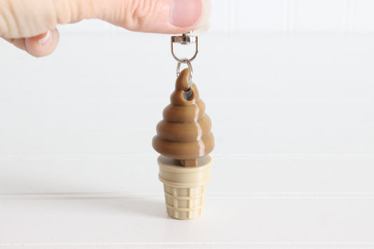Hand holding a chocolate soft-serve ice cream cone keychain to show its size.