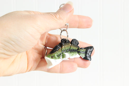 Hand holding the 3D-printed green largemouth bass keychain to show its size, colors, and silver swivel clip.