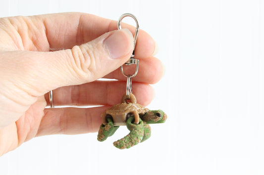 Hand holding the 3D-printed green sea turtle keychain to show its size, colors, and silver swivel clip.