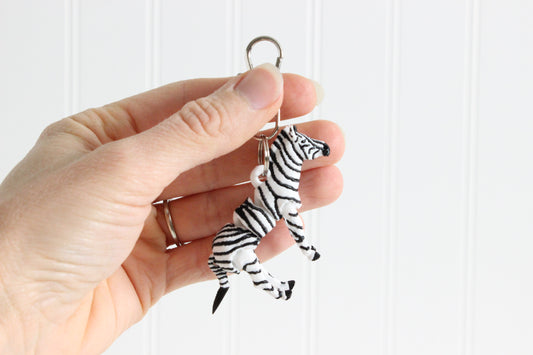 Hand holding the 3D-printed black-and-white zebra keychain to show its size, colors, and silver swivel clip.