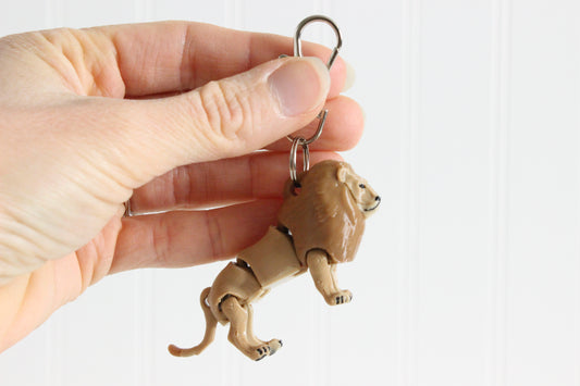 Hand holding the 3D-printed golden lion keychain to show its size, colors, and silver swivel clip.