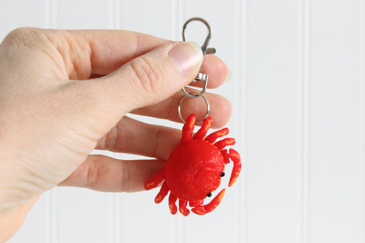Hand holding the 3D-printed red crab keychain to show its size, colors, and silver swivel clip.