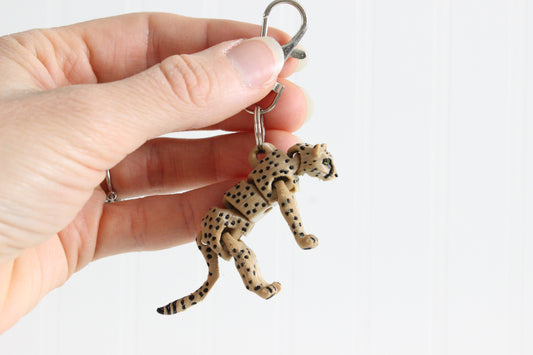 Hand holding the articulated cheetah keychain to show its spotted pattern and size.