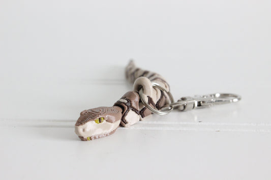 Close-up of the copperhead snake keychain showing detailed head, greenish yellow eyes, and textured scales.