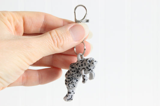 Hand holding the 3D-printed gray seal keychain to show its size, colors, and silver swivel clip.