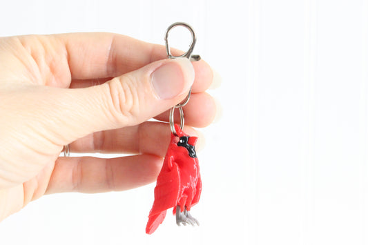 Hand holding the 3D-printed red cardinal keychain to show its size, colors, and silver swivel clip.