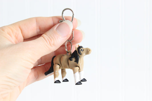 Hand holding the 3D-printed brown horse with a black mane keychain to show its size, colors, and silver swivel clip.