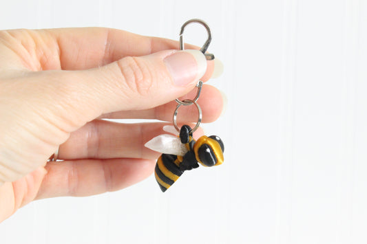 Hand holding the 3D-printed yellow-and-black bee with translucent wings keychain to show its size, colors, and silver swivel clip.