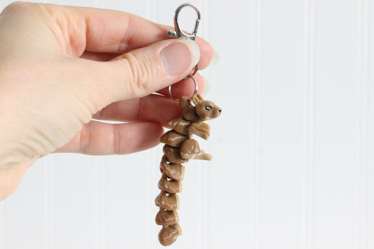 Hand holding the 3D-printed brown squirrel keychain to show its size, colors, and silver swivel clip.