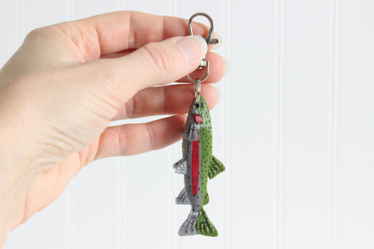 Hand holding the 3D-printed rainbow trout with a red side stripe keychain to show its size, colors, and silver swivel clip.