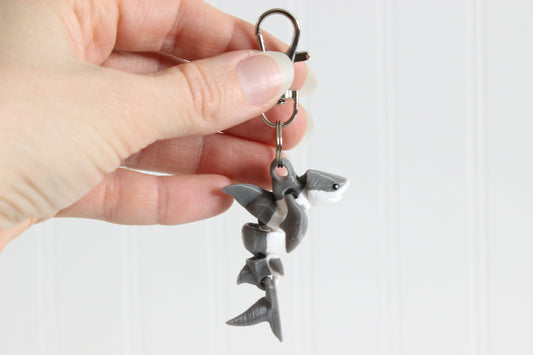 Hand holding the 3D-printed gray-and-white great white shark keychain to show its size, colors, and silver swivel clip.