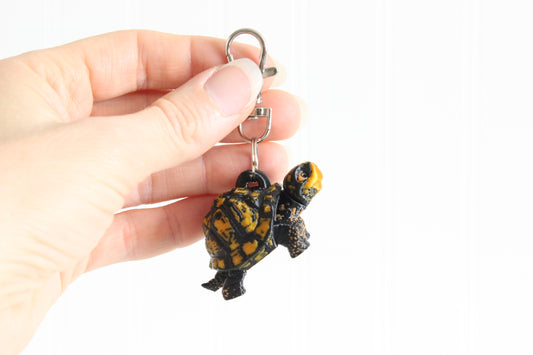 Hand holding the 3D-printed brown-and-gold box turtle keychain to show its size, colors, and silver swivel clip.