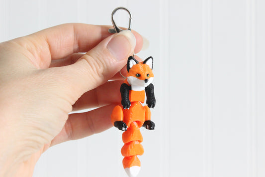 Hand holding the 3D-printed orange-red fox keychain to show its size, colors, and silver swivel clip.