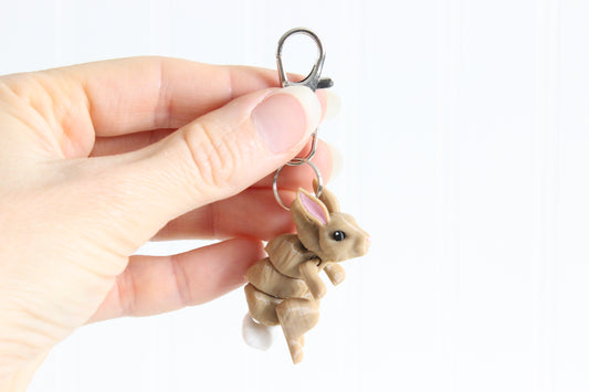 Hand holding the 3D-printed brown rabbit keychain to show its size, colors, and silver swivel clip.