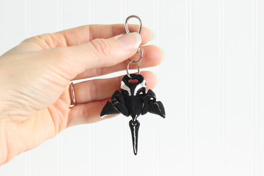 Hand holding the 3D-printed oceanic manta ray keychain to show its size, colors, and silver swivel clip.