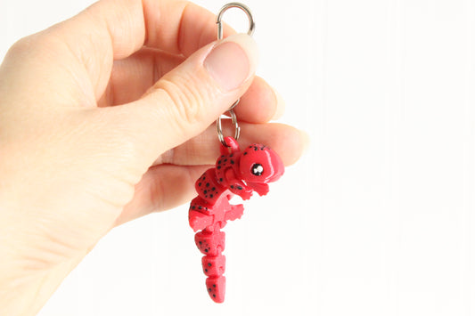 Hand holding the 3D-printed red salamander keychain to show its size, colors, and silver swivel clip.