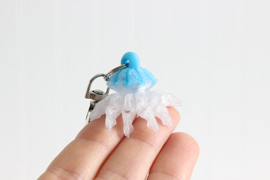Hand holding the 3D-printed jellyfish keychain to show its size, colors, and silver swivel clip.