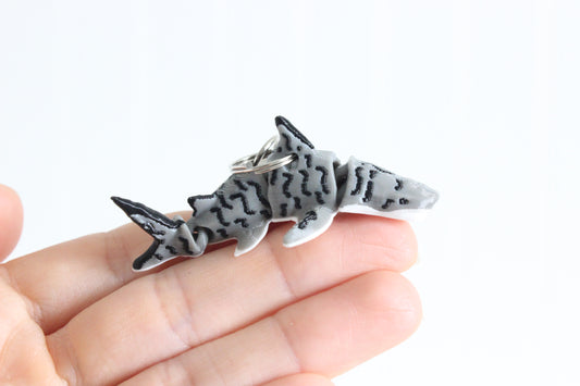 Hand holding the 3D-printed striped tiger shark keychain to show its size, colors, and silver swivel clip.
