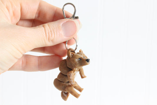 Hand holding the 3D-printed brown grizzly bear keychain to show its size, colors, and silver swivel clip.