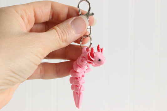 Hand holding a pink 3D-printed axolotl keychain to show its size and external gills.