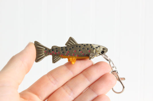 Hand holding the 3D-printed brown trout with spotted markings keychain to show its size, colors, and silver swivel clip.