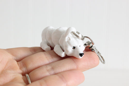 Hand holding the 3D-printed white polar bear keychain to show its size, colors, and silver swivel clip.