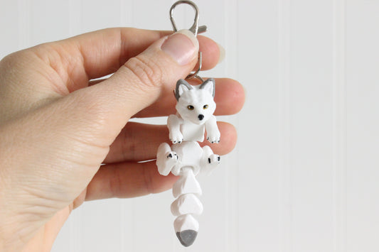 Hand holding the 3D-printed white Arctic fox keychain to show its size, colors, and silver swivel clip.