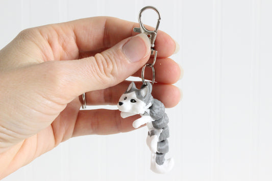 Hand holding the 3D-printed gray-and-white husky keychain to show its size, colors, and silver swivel clip.