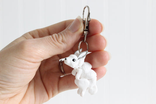Hand holding the 3D-printed white snow rabbit keychain to show its size, colors, and silver swivel clip.