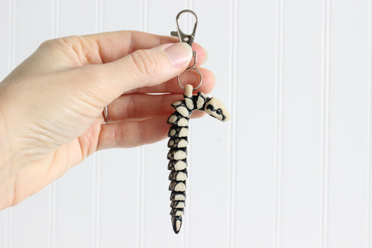 Hand holding an articulated boa constrictor snake keychain with black and cream scale pattern and swivel quick-clip key ring