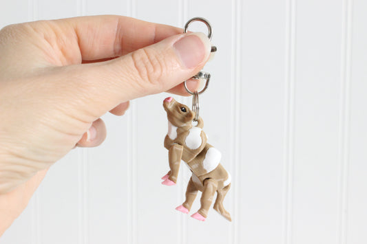 Hand holding the 3D-printed brown-and-white cow keychain to show its size, colors, and silver swivel clip.