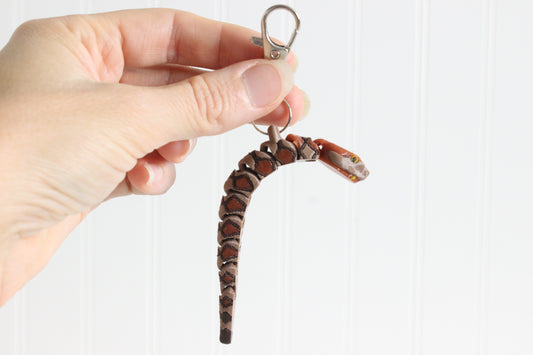 Hand holding the articulated copperhead snake keychain for size reference.