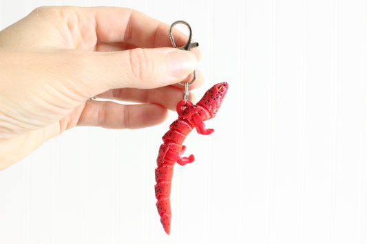 Hand holding the 3D-printed red salamander keychain to show its size, colors, and silver swivel clip.