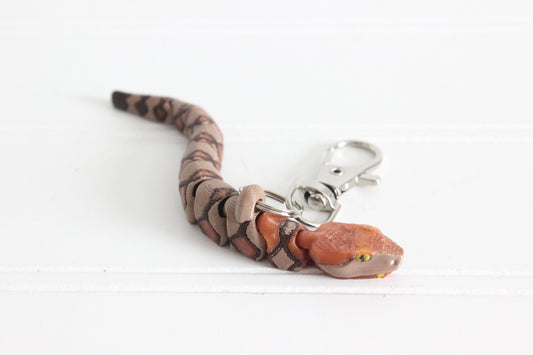 Close-up of the copperhead snake keychain showing detailed head, greenish yellow eyes, and textured scales.